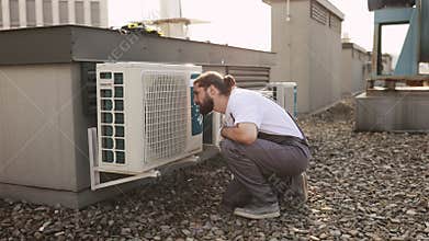 Man construction crouching and examining conditioner on roof