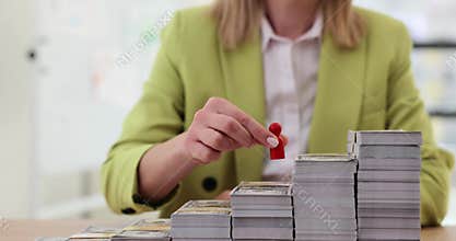 Businesswoman builds a ladder to success with the help of money stacks and a man figurine