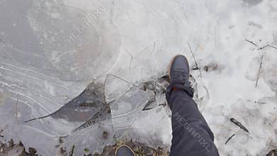 a man in black shoes breaks thin ice on puddles in the park, thin transparent ice on a puddle in the park on a winter
