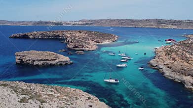 Boats floating in the crystal clear turquoise sea water. Blue lagoon, Comino, Maltese Islands. Aerial statick shot