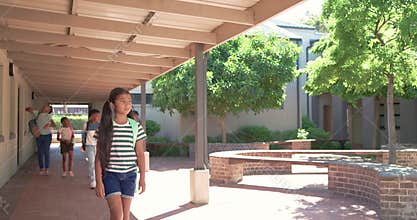 Diverse classmates entering walkway between classes, striped girl leading, walking with backpacks