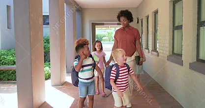 African American teacher guiding kids to sunlight through covered hall, holding tablet, backpacks
