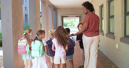 African American teacher guiding six youth, touching backpacks and holding tablet toward outdoors