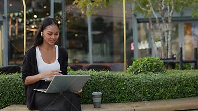 Portrait of joyful Asian woman waves hand on video call via laptop on street