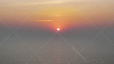 Serene aerial view of a hazy sunset over a calm ocean, with the sun\'s reflection shimmering on the water\'s surface