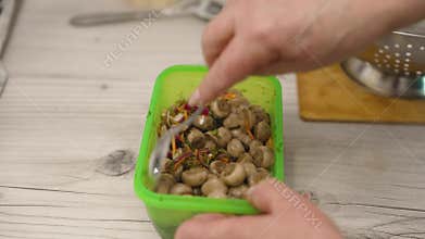 Chef combining marinated mushrooms with vegetables in food container