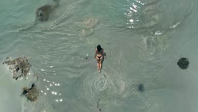 Aerial view of a woman in a black bikini walking through shallow turquoise water on a sunny day at the beach vacation vibes
