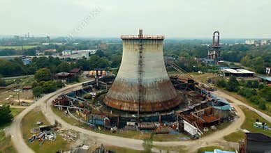 Aerial view of an abandoned industrial cooling tower surrounded by decaying infrastructure on an overcast day in europe