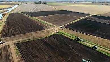 Aerial view of agricultural fields with tractors working the land near a winding river