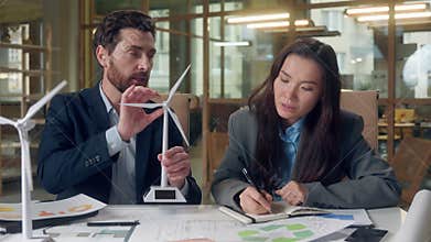 Windmill design agriculture discussion Caucasian man explains model Korean woman takes notes writing notebook green
