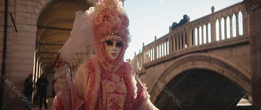 Portrait of woman in gorgeous dress with pink lace and mask walks by bridge