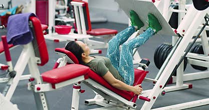 A middle-aged woman trains her leg muscles with the leg press machine. 4k video.