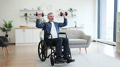 Mature man in wheelchair lifting dumbbells in modern living room