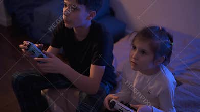 Siblings gaming on console together in the evening at home