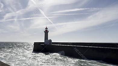 Lighthouse standing on a concrete pier extending into the ocean