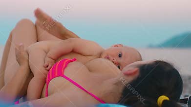 Mother breastfeeding little baby boy at beach. Baby feeding from mother breast