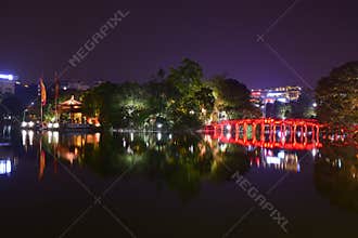 Night view with water reflection of The Huc Bridge in bright red with Ngoc Son Temple, Hanoi, Vietnam.