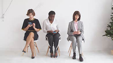 Three business girls expect interviews sitting on chairs in the hallway of an office building.