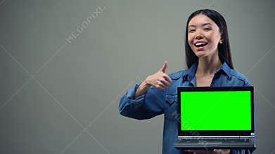 Smiling woman showing thumbs-up holding green screen laptop, online education