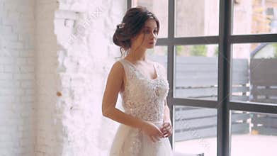 Girl in a light white luxurious wedding dress poses, stands alone in a spacious room, the interior is in a Scandinavian
