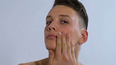 Man applying moisturizing cream on face and smiling, home spa treatment skincare
