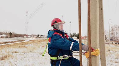 Electrician in helmet elevated to power line using belt at pole
