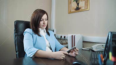 Businesswoman brunette in a blue jacket sat down in her chair in the office and started to work on the keyboard.