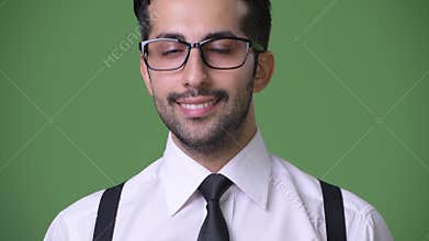 Young handsome bearded Persian businessman against green background