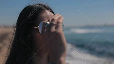 The sea, the foamy waves, and the beach reflect in the shades of an attractive dark-haired girl