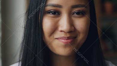 Close-up slowmotion portrait of charming Asian girl with dark eyes, perfect skin with make-up and white teeth looking at