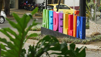 Colorful Medellin sign at street with traffic and green leaves