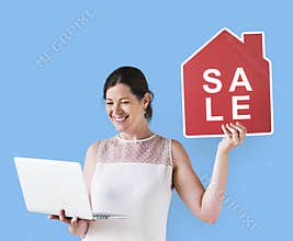 Woman holding a house sale icon and using a laptop