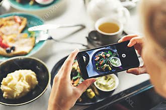 Woman with smart phone taking picture of food at restaurant
