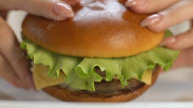 Woman biting big fast food burger, gaining extra weight, saturated fat, closeup