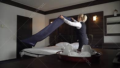 Maid makes a double bed in a small, cozy hotel room.