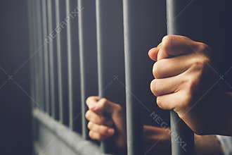 Man in prison hands of behind hold Steel cage jail bars.