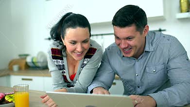 Caucasian couple is using computer at kitchen. Home, technology and relationships concept - smiling husband and wife