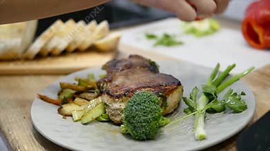 Woman puts a meat steak and vegetables on a plate