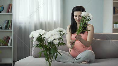 Lovely pregnant girl decorating house with nice flowers, aesthetic enjoyment