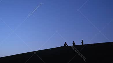 Silhouettes of Three Guys making Photo on Smartphone and Selfie on the Slope of Hill Early in the Morning with Young