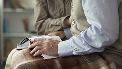 Aged couple opens photo album on lap to look at pictures together, reminiscence