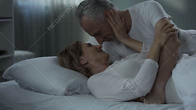 Senior man and woman lying in bed and nuzzling, happily married, tenderness