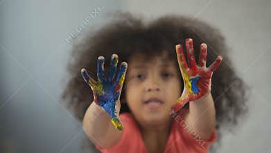 Cheerful Afro-American girl having fun and showing painted palms into camera