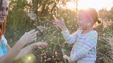 Mom and daughter having fun and blowing Dandelion seeds while relaxing at nature