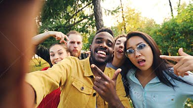 Point of view shot of friends taking selfie in park looking at camera, making funny faces and laughing having fun