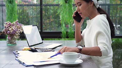 Beautiful young strain asian woman working on laptop while unhappy using smartphone in living room at home.
