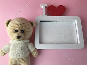 Soft knitted bear on a pink background with a cute frame in white. a bear with black eyes made of beads lies and looks at a