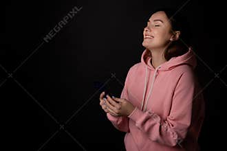 Cute young brunette in a pink hoodie uses a smartphone and laughs, communication without borders,