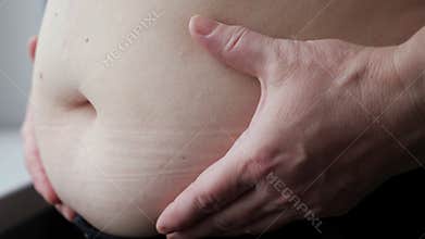 Mature woman strokes and squeezes fat belly near windowsill