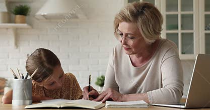 Smiling older mature grandmother helping little child girl with study.
